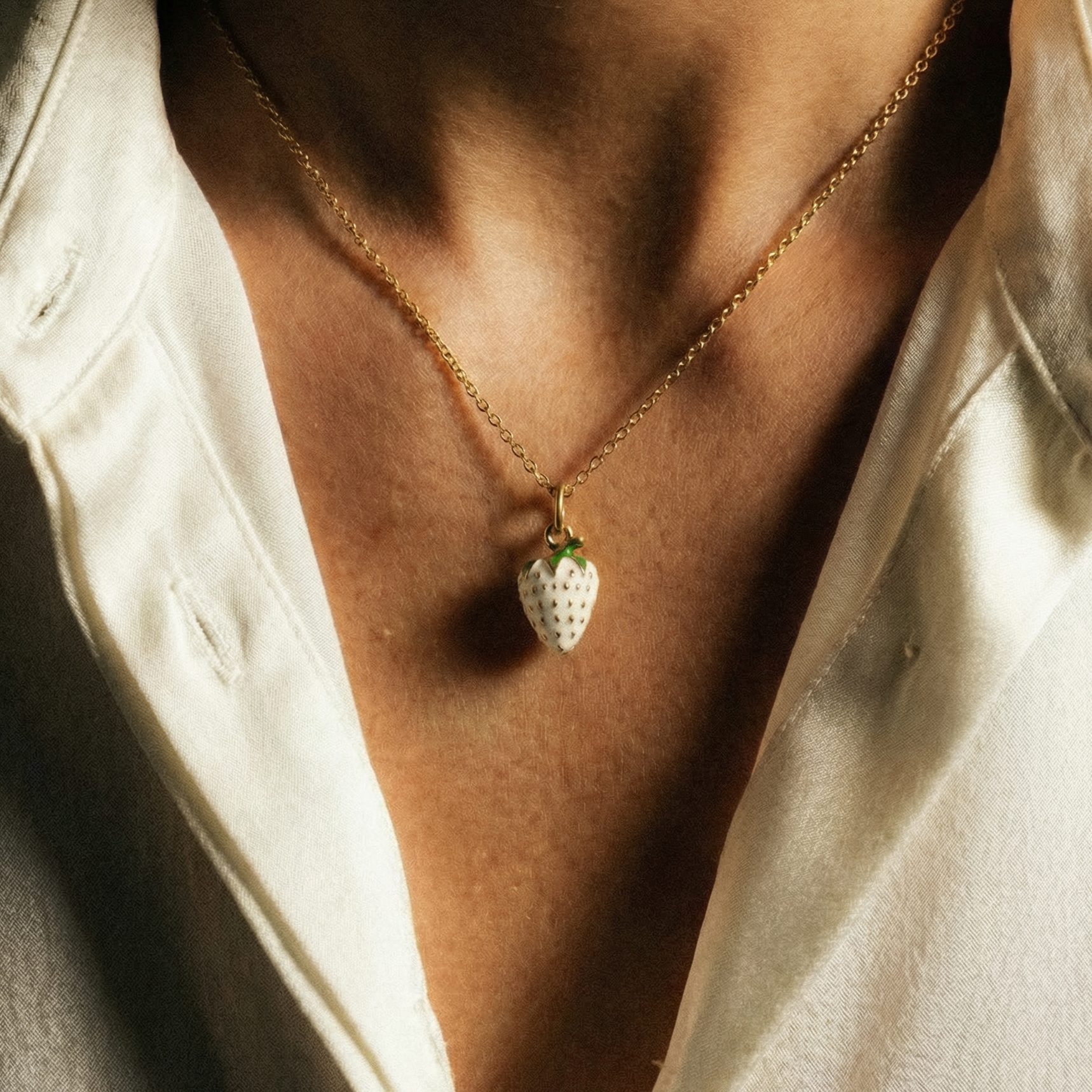 Necklace with a strawberry pendant worn by a person in a light-colored shirt.